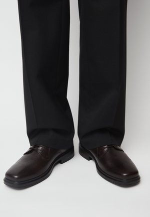 Dunkelbraune Lederschuhe, getragen mit schwarzen formellen Hosen auf einem schlichten hellen Hintergrund.