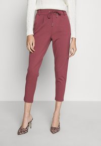 Pantaloni a sigaretta bordeaux con vita regolabile e tasche laterali, caratterizzati da una texture liscia. Abbinati a décolleté a punta con stampa leopardata.