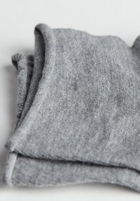 Pieza de tela gris con una textura suave, que presenta un diseño plegado y bordes cosidos, creando una forma rectangular plana y simple.