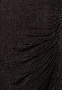 Lähellä mustaa kangasta, jossa on kerroksellinen rypytetty pinta, joka luo viistosti taitteita ja varjoja.