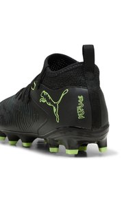 Botín de fútbol negro con un diseño texturizado, que presenta un logo de PUMA y la marca "Play Free Future" en verde brillante en el talón.