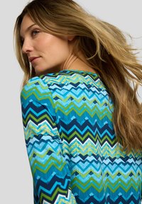 Langärmliges Oberteil mit einem mehrfarbigen Zickzackmuster in Blau- und Grüntönen, gefertigt aus einem strukturierten Stoff. Abgerundeter Ausschnitt und lockere Passform.