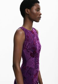 Robe sans manches violette avec des motifs floraux, une silhouette ajustée et un tissu texturé avec un léger ruché sur le côté.
