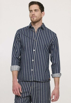 Chemise à rayures bleu marine avec manches grises retroussées ; dotée de boutons argentés et d'un col. Fabriquée à partir d'un tissu texturé.