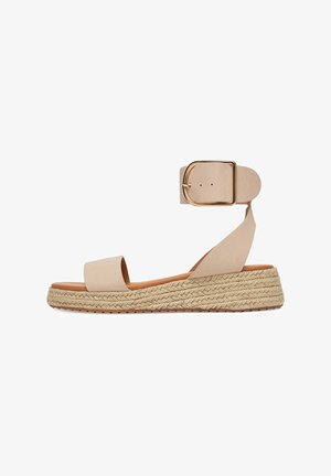 Beige Flache Sandale mit breiter Vorderriemen, geflochtenem Seilsohle und Knöchelriemen mit einer großen goldenen Schnalle.