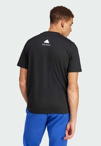 T-shirt en coton noir à manches courtes, affichant un logo blanc dans le haut du dos et une coupe régulière, associé à un pantalon bleu.