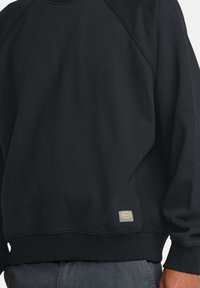 Czarny sweatshirt wykonany z miękkiego materiału, z ryflowanym kołnierzem i mankietami, z małą haftowaną metką u dołu. Prosty, gładki design.