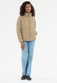 Beige dunjakke med høj krave og horisontale syninger, kombineret med lyseblå jeans og sorte sko.