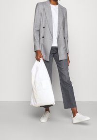 Blazer grigio a doppio petto, t-shirt bianca, jeans grigi, con una borsa puffa bianca e sneakers bianche; tessuti morbidi e vestibilità su misura.
