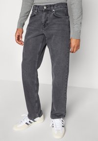 Jeans in denim grigio scuro con vestibilità rilassata, dotati di cinque tasche, chiusura a bottone e leggere scoloriture. Abbinati a sneaker bianche.
