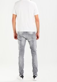 Grå jeans med slim fit, med en sliten design, färgsplatterdetaljer och femfickorsstil. Bärs med en enkel vit t-shirt.