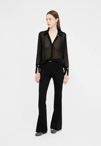 Juoda permatoma palaidinė su sagomis ir ilgomis rankovėmis, derinama su aptemptomis juodomis praplėstomis kelnėmis. Lygus audinys, minimalistinis dizainas ir subtilios detalės.