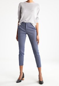 Light gray knit sweater with a relaxed fit; blue patterned trousers with cropped legs; black heels with wooden block heels.