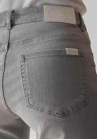 Jeans in denim grigio con una texture liscia e un dettaglio sulla tasca posteriore. Un'etichetta bianca con il marchio è visibile sulla cintura.