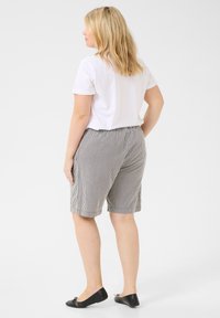 Shorts en tissu rayé noir et blanc, taille élastique, coupe au niveau des genoux ; associés à un t-shirt décontracté blanc à manches courtes et des ballerines noires.