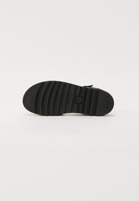 Svart såle til sandaler med en teksturert, ribbet overflate; har strukturerte spor og en sentral logo; laget av slitesterkt gummimateriale.