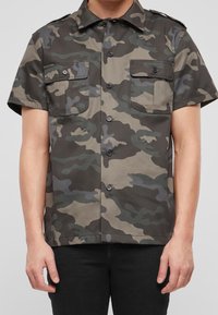 Camicetta a maniche corte con bottoni in un motivo di camouflage multicolore. Presenta due tasche sul petto e un colletto. Realizzata in tessuto resistente.