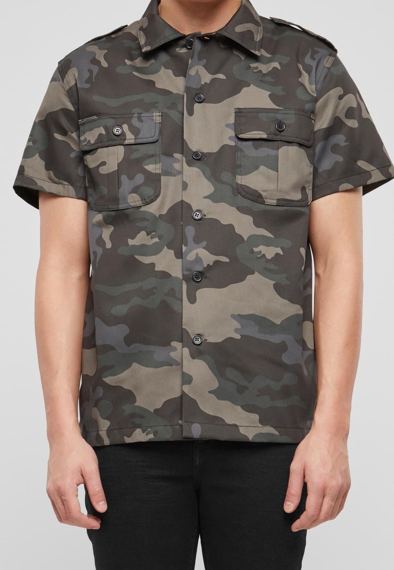 Camicetta a maniche corte con bottoni in un motivo di camouflage multicolore. Presenta due tasche sul petto e un colletto. Realizzata in tessuto resistente.