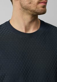 Marineblauwe gestructureerde sweater met een ruitpatroon, geribbelde halslijn en zacht materiaal, waarbij een deel van de nek en kin zichtbaar is.
