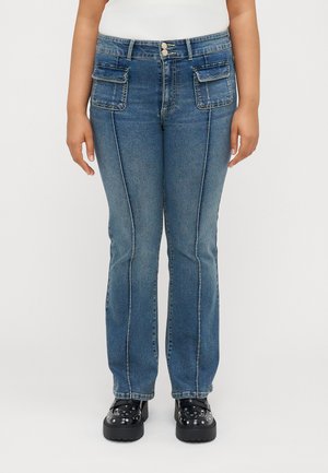 Blue denim jeans with a high waist, two front pockets, and contrast stitching. Paired with black platform shoes featuring studs.