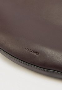 Pruun nahast ümmargune kotike tekstureeritud viimistlusega, millel on peened õmblused ja reljeefne logo. Sile pind tumedate aktsentääridega servadel.