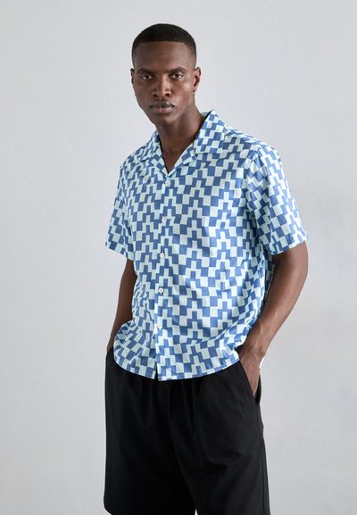 Chemise à manches courtes à boutons avec un motif géométrique bleu et bleu clair, fabriquée en tissu léger, avec une coupe décontractée et un col ouvert.