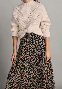 Crème gebreide trui met een hoge halslijn en een gestructureerd patroon, gecombineerd met een lange zwarte rok met een lichtbruine luipaardprint.
