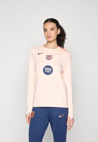 Hosszú ujjú, világos őszibarack színű sporting, sima anyagból; elöl tengerészkék logóval és Spotify grafikával rendelkezik, narancssárga kiegészítőkkel.