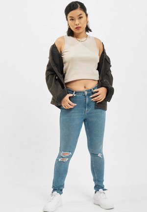 Blå ripped skinny jeans med høyt liv, kombinert med en beige ribbet crop topp og en oversized svart denimjakke. Hvite sneakers.