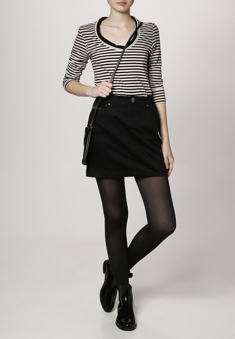 Blusa de rayas de manga larga con cuello redondo, combinada con una falda de mezclilla negra. La modelo lleva pantis negros y botas de tobillo, sosteniendo un bolso pequeño.