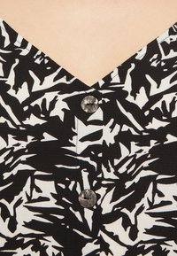 Zwart-wit gepatternde top met een V-halslijn, een enkele decoratieve knop en een textuurstof met organische vormen.