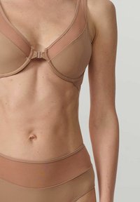 Reggiseno beige con una texture liscia, supporto con stecche, e chiusura frontale. Abbinato a underwear alta in vita coordinata, entrambi senza cuciture.