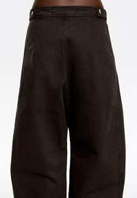 Pantalones negros de tiro alto, hechos de tejido texturizado; cuentan con un bolsillo lateral, cierre de botón y piernas anchas y relajadas.