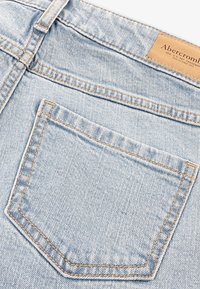 Jeans in denim azzurro chiaro con tasca posteriore con cuciture arancioni e un'etichetta in pelle in vita. La texture appare liscia e consumata.