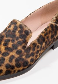 Chaussure plate à imprimé léopard en fourrure douce, avec un design ajouré, un intérieur beige et une semelle basse en plastique noir.