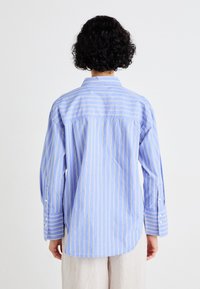 Camicia a maniche lunghe button-up a righe blu con accenti gialli, dotata di colletto e realizzata in un tessuto leggero. La vista posteriore mostra una vestibilità rilassata.