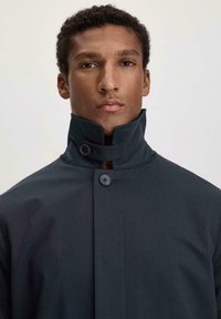 Dunkelgrauer Mantel mit hohem Kragen, ausgestattet mit zwei vorderen Knöpfen und einem glatten, strukturierten Stoff. Keine sichtbaren Muster oder Verzierungen.