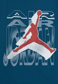 Tyrkysové tričko s červenou siluetou skákající postavy. Text zní "AIR JORDAN" v bílém a šedém zkresleném písmu.