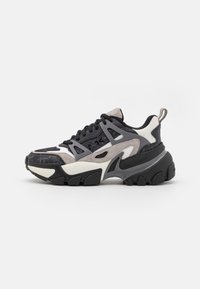 Des baskets noires et grises robustes présentent un mélange de matériaux, y compris du daim et du mesh, avec un motif texturé et une semelle épaisse et superposée.