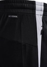 Shorts deportivos negros con una tela texturizada, panel lateral blanco en contraste, cintura elástica y un pequeño bolsillo con cremallera.