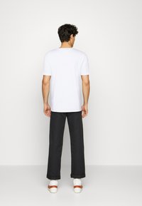 T-shirt bianco a maniche corte, pantaloni neri a gamba larga e scarpe bianche con una cintura marrone. Texture liscia, design minimalista. Vista posteriore.