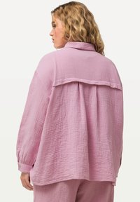 Jasnoróżowa, oversize koszula wykonana z teksturowanej tkaniny, z kołnierzykiem, plisą z tyłu i guzikami przy mankietach. Charakteryzuje się luźnym krojem i miękkim designem.