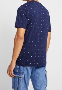 Navy blue cotton t-shirt with a pattern of small white squares and dots. Short sleeves and a crew neck design.