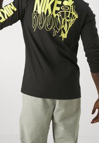 Felpa nera a maniche lunghe con grafica e elementi di design in giallo neon, abbinata a pantaloni sportivi grigi chiari. Tessuto di texture liscia.