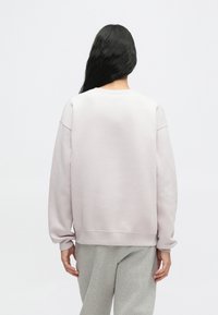 Ανοιχτό γκρι φούτερ με στρογγυλή λαιμόκοψη και μακριά μανίκια, με απαλό υλικό και χαμηλούς ώμους. Συνδυασμένο με γκρι παντελόνια φόρμας.