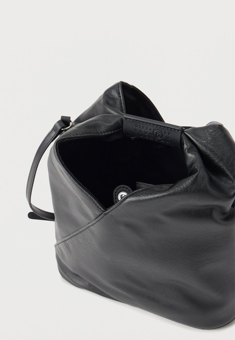 Sac à bandoulière en cuir noir doux avec ouverture supérieure, fermeture à bouton-pression visible et strap fin réglable sur fond blanc.