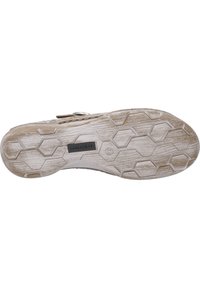 Die Sohle des Sneakers weist eine strukturierte GummOberfläche mit sechseckigen Mustern auf, ist überwiegend weiß mit Schmutzflecken und hat ein Markenlabel.