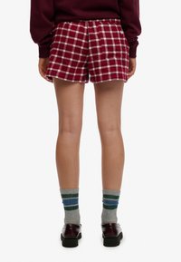 Czerwono-białe szorty w kratę z elastycznym pasem, tylne kieszenie, do tego skarpetki w paski w odcieniach szarości i zieleni oraz czarne buty.