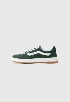Grønn semsket sneaker med hvite detaljer, hvite snøringer og en brun gummisåle. Har en lav silhuett og en teksturert overdel for bedre grep.