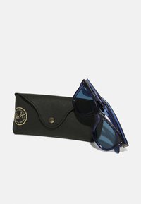 Ochelari de soare Ray-Ban din plastic translucid de culoare albastră închisă, cu lentile închise, lângă o etui din piele neagră cu un logo auriu și închidere tip capsa.